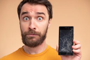 portrait shocked young man showing his broken smartphone